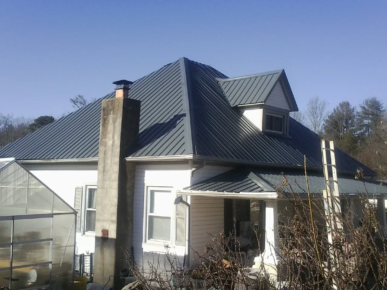 Dark blue standing seam metal roof on a white farmhouse with dormer — Slate & Tile Roof Repair by Roofing Brothers in Hurley