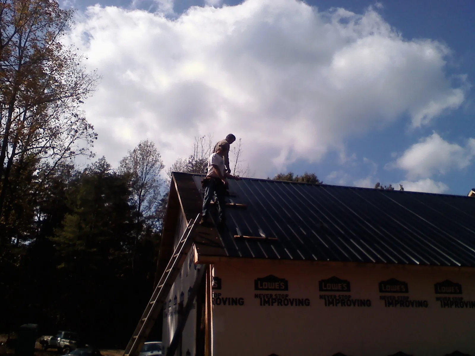 Roofer fastening dark metal panels high against a cloudy sky, from a Roof Inspection job in Hurley